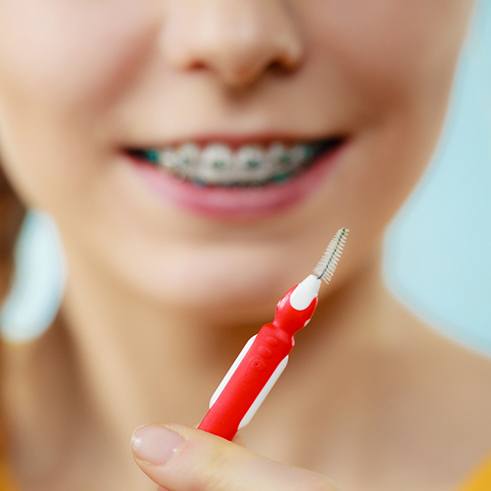 Girl with braces blurry in background holding toothbrush and interproximal brush in foreground