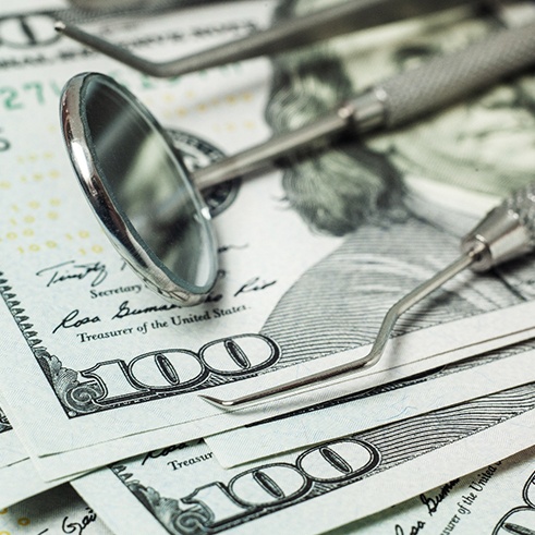 Dental instruments resting on several $100 bills. 
